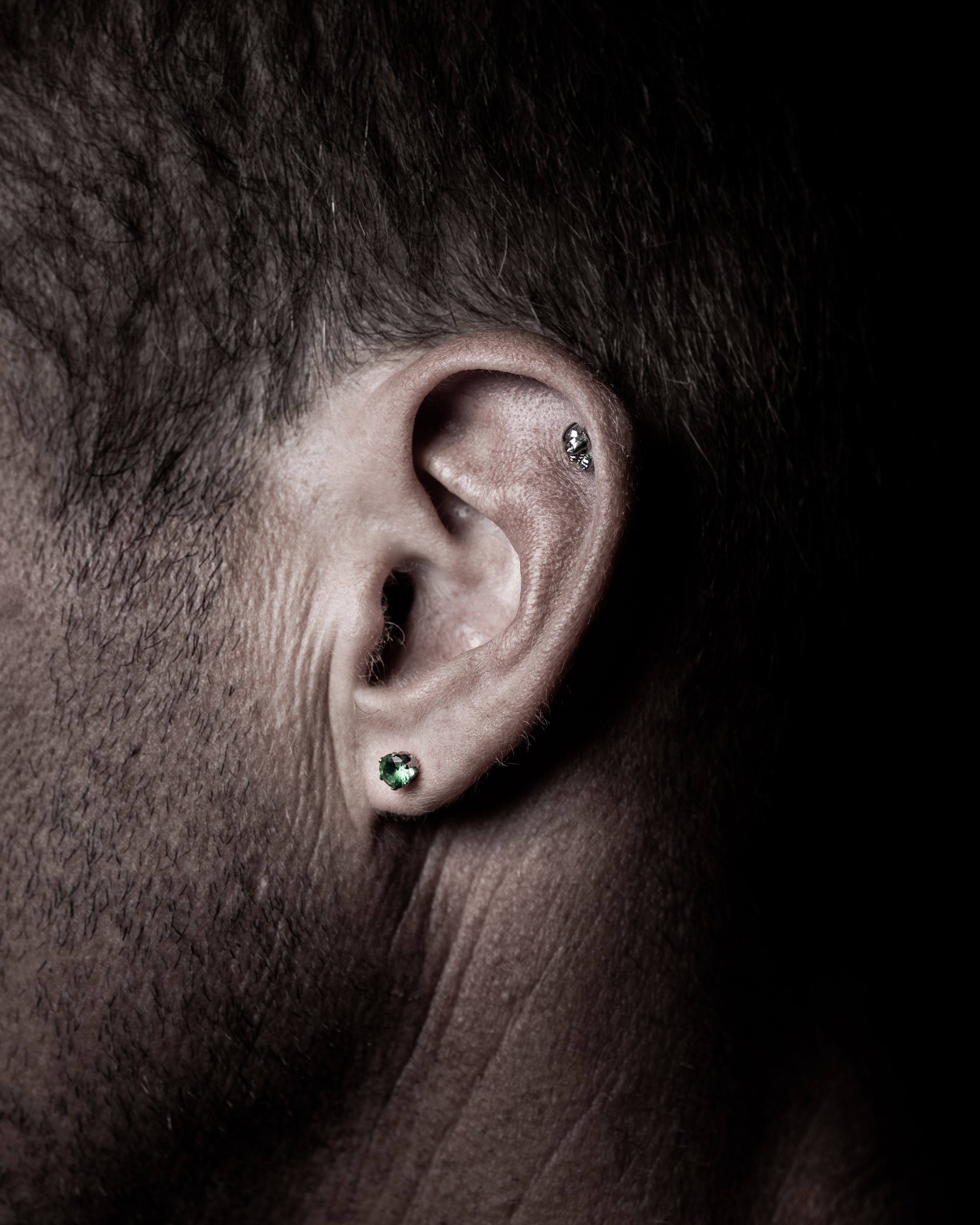 Ear with helix and lobe piercings against a dark studio backdrop